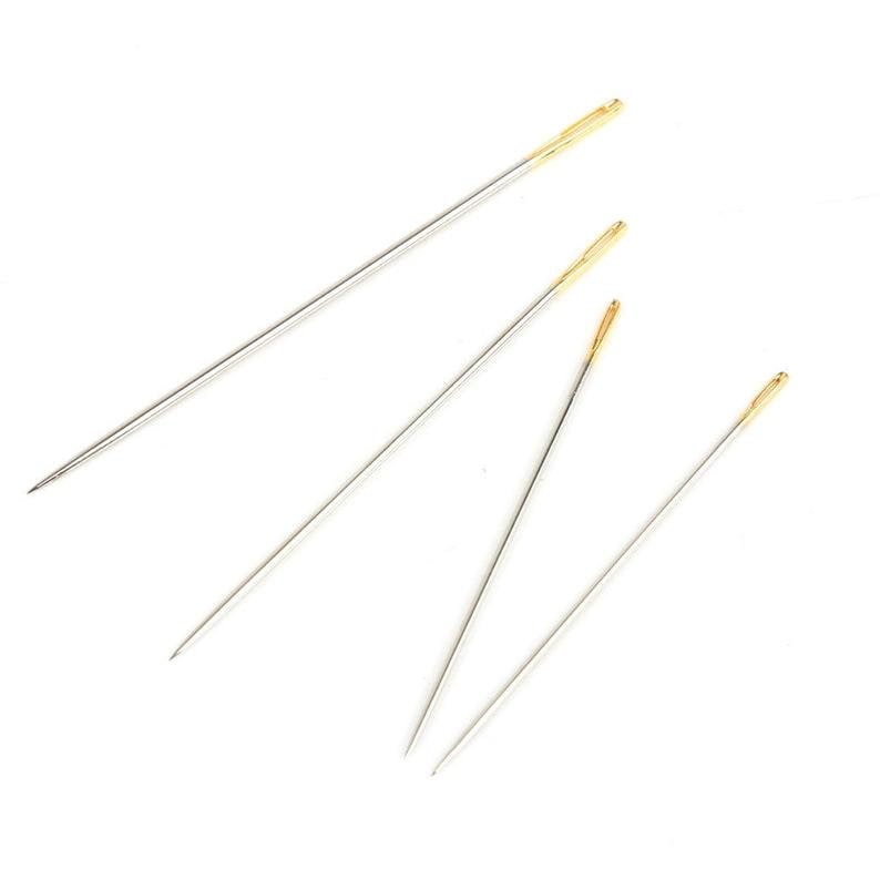May include: Four silver sewing needles with gold eye tips. The needles are arranged in a fan shape on a white background.