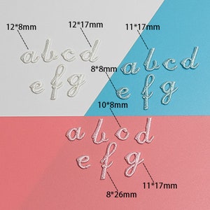 May include: White embroidered letters of the alphabet, a, b, c, d, e, f, and g, in various sizes, on a white, pink, and blue background. The letters are arranged in three rows, with the largest letters at the top and the smallest letters at the bottom. The letters are all in a cursive font.