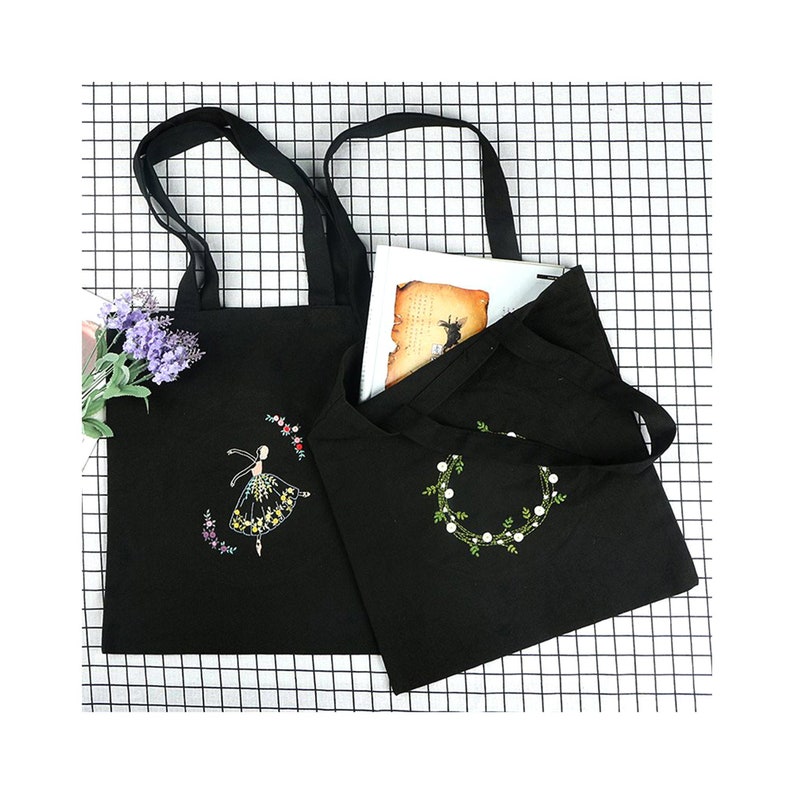 May include: Two black canvas tote bags with embroidered designs. One bag features a ballerina with floral accents, while the other has a floral wreath.