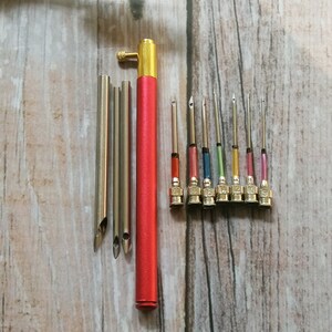 May include: A set of 10 embroidery needles with different colored tips and a red needle threader tool. The needles are numbered 1 to 10.