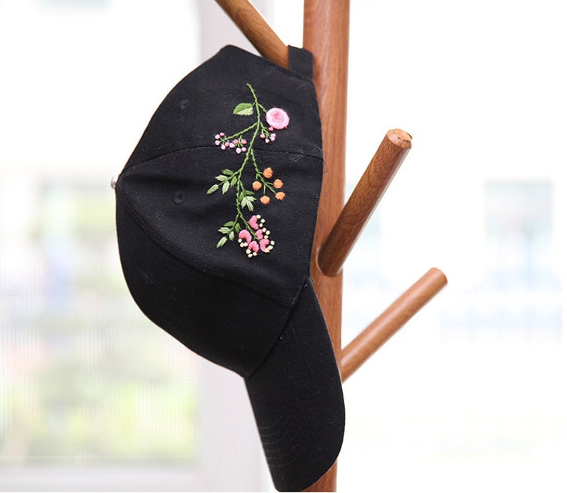 May include: A black baseball cap with an embroidered floral design in pink, green, and orange.