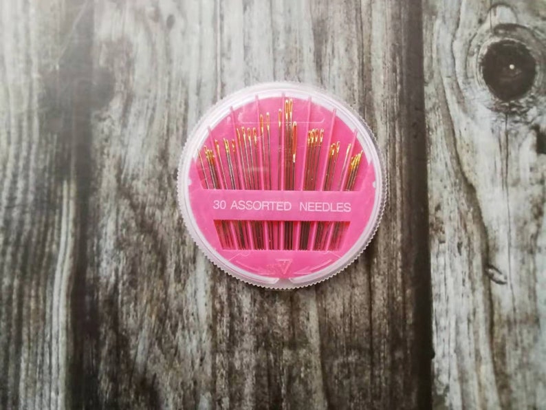 May include: A pink plastic container with a clear lid holds 30 assorted needles. The container has the text "30 Assorted Needles" printed on it.