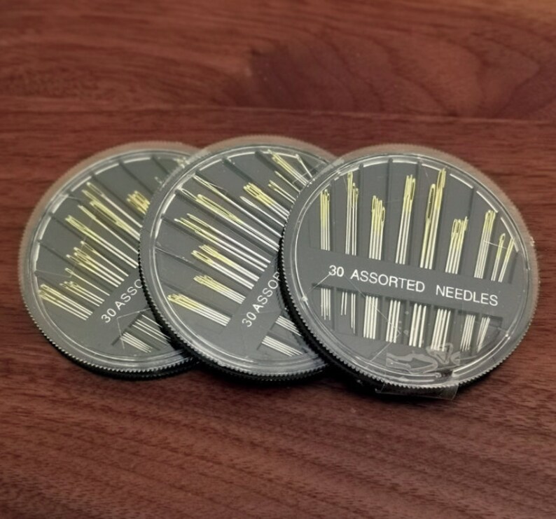 May include: Three round black plastic containers filled with assorted needles. Each container has a label that reads "30 Assorted Needles".