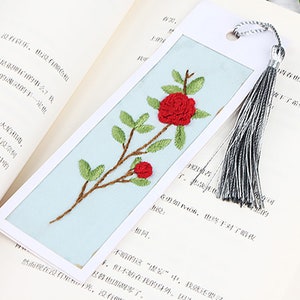 May include: A blue bookmark with a white border and a red embroidered flower design. The bookmark has a silver tassel.