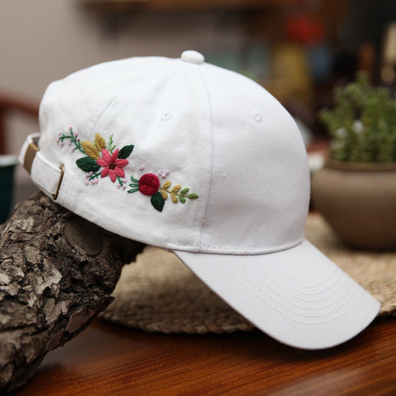 May include: White baseball cap with embroidered flowers in shades of pink, red, green, and yellow.