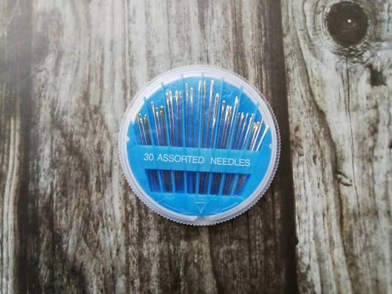 May include: A round, blue plastic container with a clear lid holds 30 assorted needles. The container has "30 ASSORTED NEEDLES" printed on it.