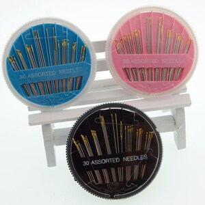 May include: Three round plastic containers with lids, each containing 30 assorted needles. The containers are blue, pink, and black.