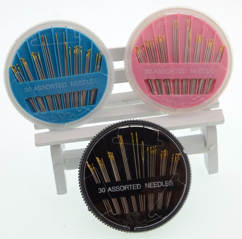 May include: Three round plastic containers with lids, each containing 30 assorted needles. The containers are blue, pink, and black.