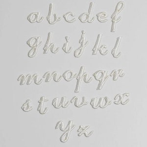 May include: White felt letters of the alphabet in a cursive font. The letters are arranged in rows, starting with "a" and ending with "z".