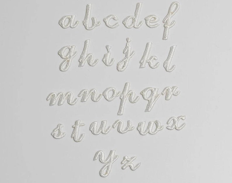 May include: White felt letters of the alphabet in a cursive font. The letters are arranged in rows, starting with "a" and ending with "z".