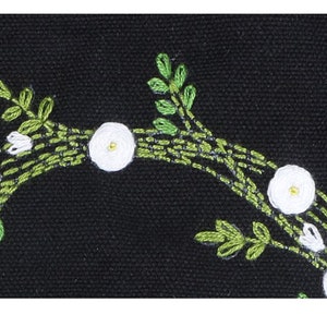 May include: Close-up of a black fabric with white flowers and green leaves embroidered on it. The flowers are simple and have a yellow center.