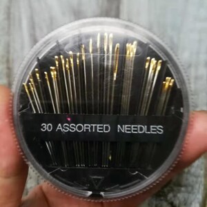 May include: A clear plastic container with a black lid holds 30 assorted needles. The container has a black label that reads "30 Assorted Needles".