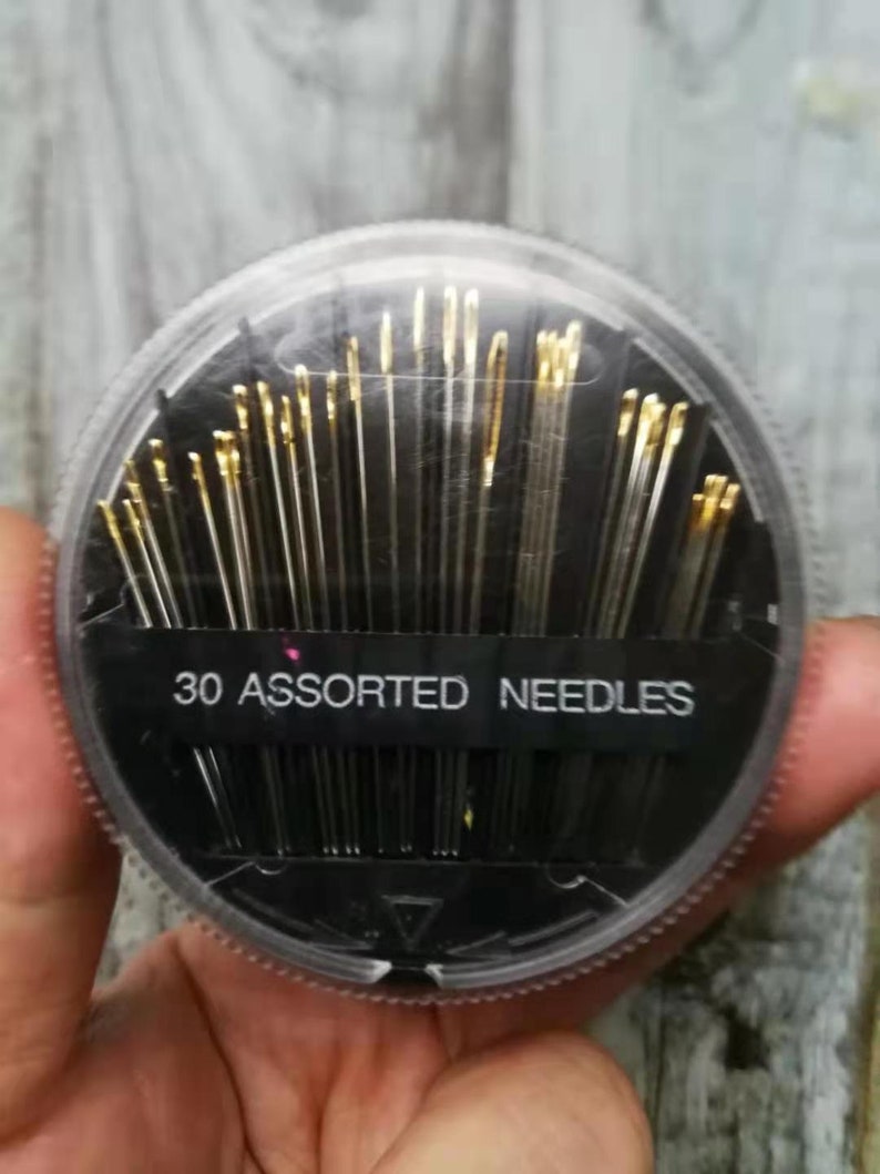 May include: A clear plastic container with a black lid holds 30 assorted needles. The container has a black label that reads "30 Assorted Needles".