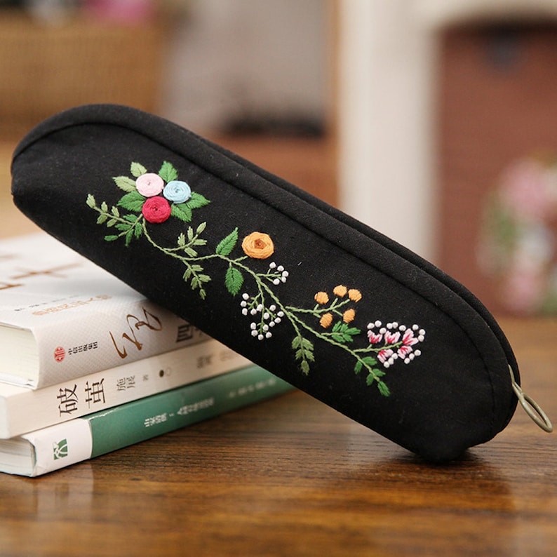 May include: Black fabric pencil case with an embroidered floral design in shades of pink, green, yellow, and white.