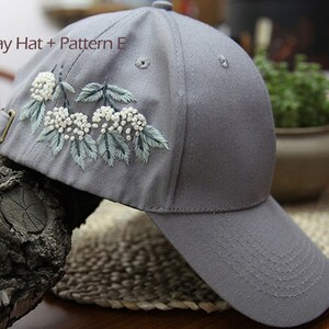 May include: Gray baseball cap with a white floral embroidery design. The embroidery features white flowers and green leaves.
