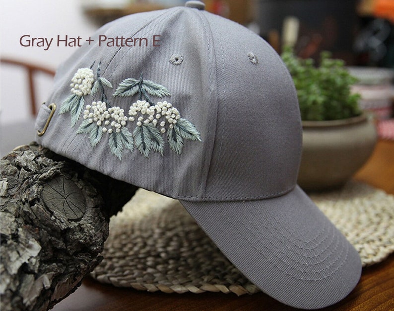 May include: Gray baseball cap with a white floral embroidery design. The embroidery features white flowers and green leaves.