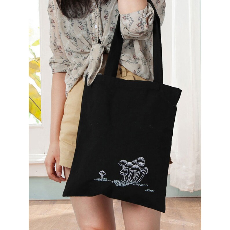 May include: A black tote bag with white embroidered mushrooms. The bag has two long straps.