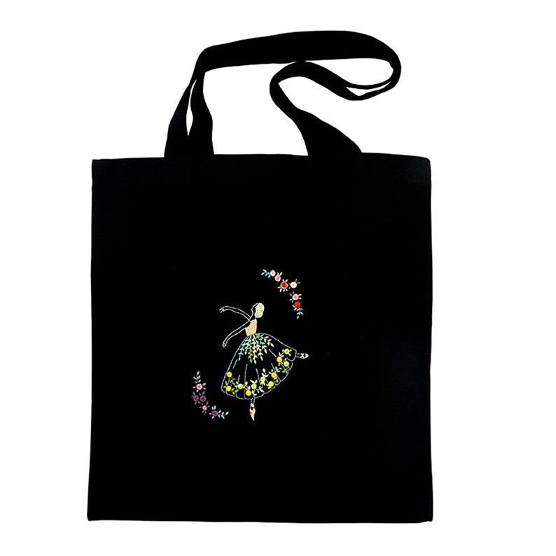 May include: Black tote bag with a ballerina design. The embroidered image features a ballerina in a floral dress, surrounded by a floral wreath. The bag has black handles and is made of a sturdy fabric.