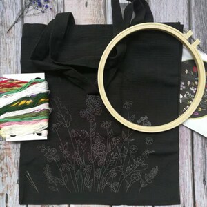 May include: A black tote bag with a floral embroidery design. The bag is being prepared for embroidery with a hoop, needles, and embroidery floss.