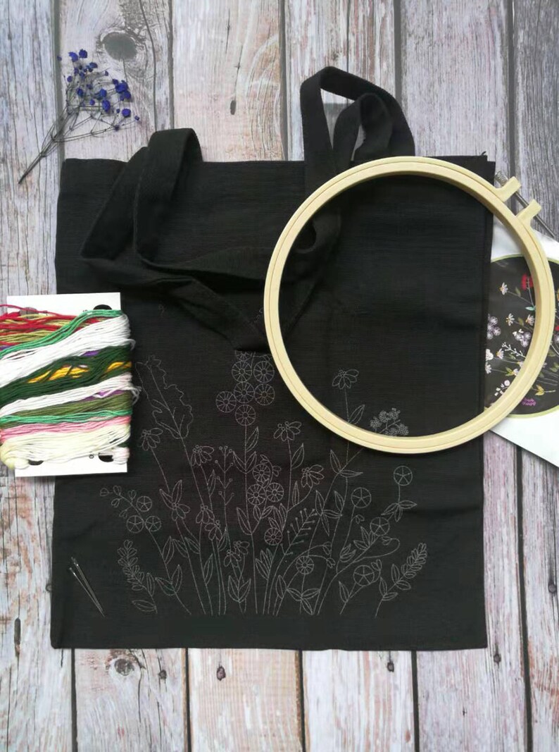 May include: A black tote bag with a floral embroidery design. The bag is being prepared for embroidery with a hoop, needles, and embroidery floss.