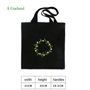 May include: Black canvas tote bag with a white and green embroidered floral wreath design. The bag has black handles and measures 31 inches wide, 36 inches high, and the handles are 28.5 inches long.