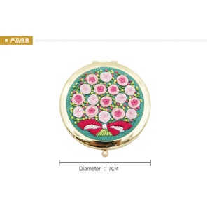 May include: A gold-toned compact mirror with a round, green embroidered design of pink roses and a red bow. The mirror has a diameter of 7 cm.