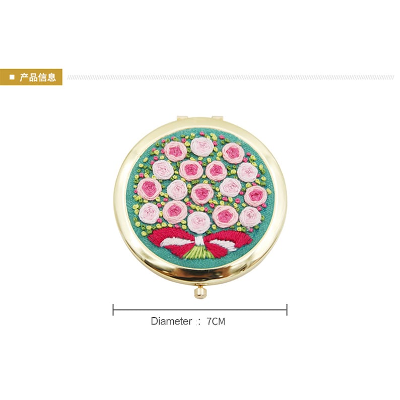 May include: A gold-toned compact mirror with a round, green embroidered design of pink roses and a red bow. The mirror has a diameter of 7 cm.