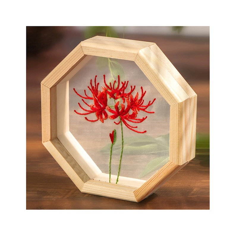 Peut inclure: Une fleur rouge brod&eacute;e dans un cadre octogonal en bois. La fleur est un groupe de fleurs rouges avec de longs p&eacute;tales fins. Le cadre est en bois brun clair et a un fond blanc.