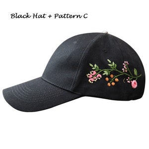 May include: Black baseball cap with a floral embroidery design. The embroidery features pink flowers, green leaves, and orange berries.