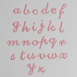 May include: Pink felt letters of the alphabet in a cursive font. The letters are arranged in rows, starting with "a" and ending with "z".