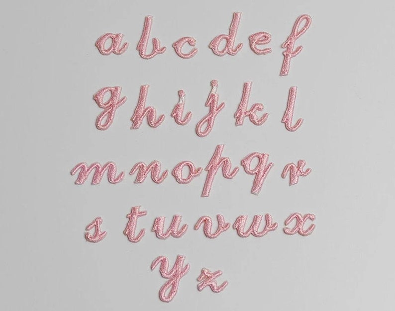 May include: Pink felt letters of the alphabet in a cursive font. The letters are arranged in rows, starting with "a" and ending with "z".