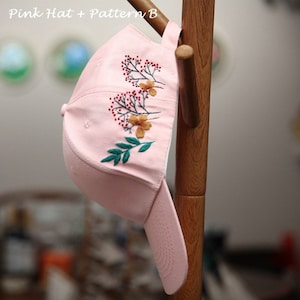 May include: A pink baseball cap with an embroidered floral design. The design features green leaves, red berries, and yellow flowers.