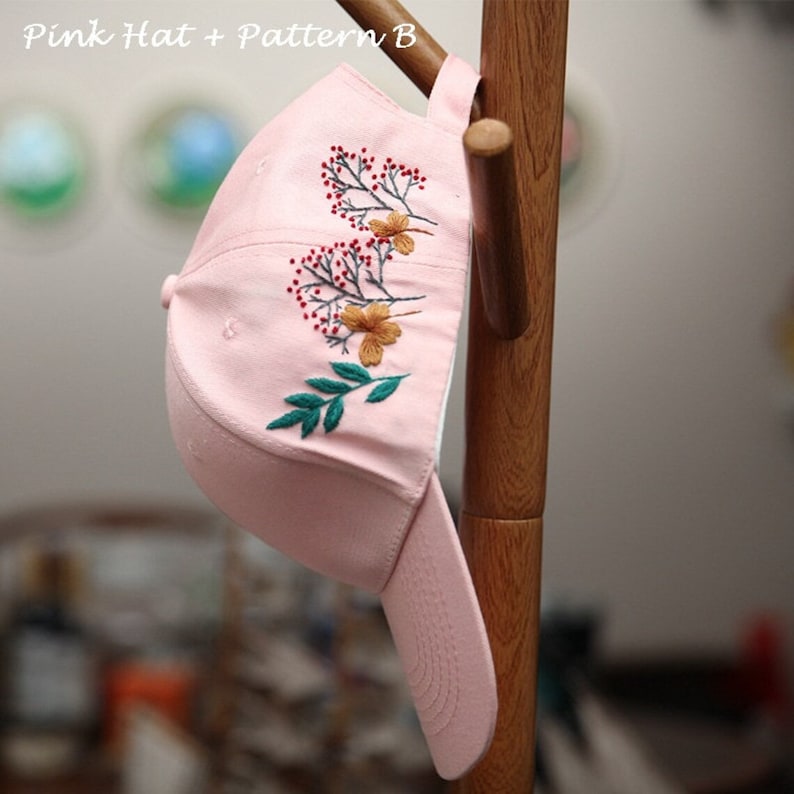 May include: A pink baseball cap with an embroidered floral design. The design features green leaves, red berries, and yellow flowers.