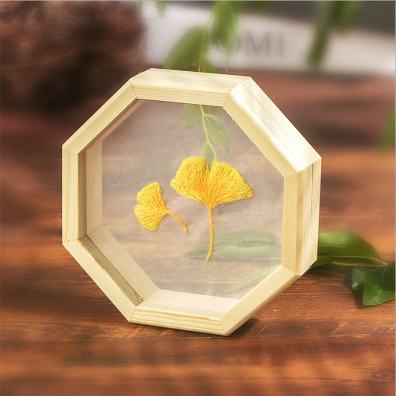 Peut inclure: Un cadre octogonal en bois avec un devant en verre transparent, mettant en valeur deux feuilles de ginkgo brod&eacute;es jaunes sur un fond blanc.