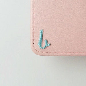 May include: A light pink leather wallet with a light blue embroidered letter "L" on the front.
