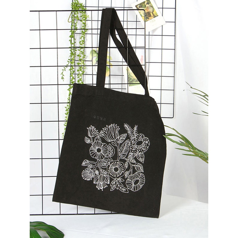 May include: Black canvas tote bag with a white floral design. The design features a variety of flowers and leaves.