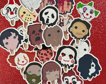May include: A collection of 18 horror movie character stickers, each featuring a different character's face on a popsicle stick. The stickers are colorful and feature characters like Jason Voorhees, Freddy Krueger, and Michael Myers.