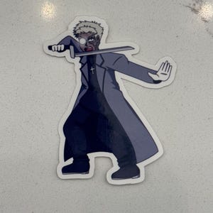 Puede incluir: Una pegatina de un personaje de dibujos animados con cabello rubio, que lleva un abrigo negro y sostiene una espada. El personaje tiene un ojo blanco y un ojo negro.