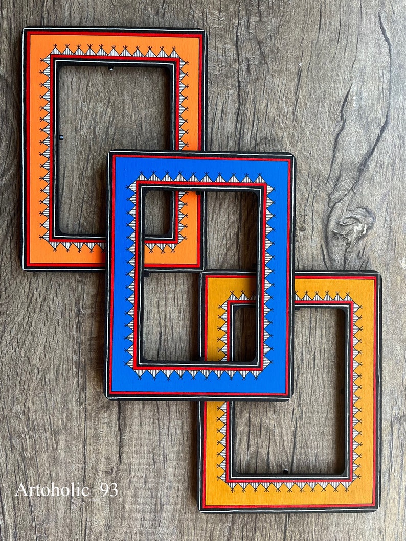 Op de afbeelding: Drie houten fotolijsten met ingewikkelde geometrische ontwerpen. De lijsten zijn in elkaar genest, met de grootste lijst oranje, de middelste lijst blauw en de kleinste lijst oranje.
