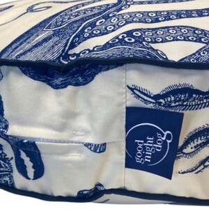May include: A white and blue dog bed with an octopus and other sea creatures printed on it. The bed has a blue border and a "good night dog" logo on the side.