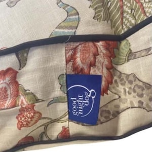 May include: A beige dog bed with a floral print and a blue label that says "good night dog".