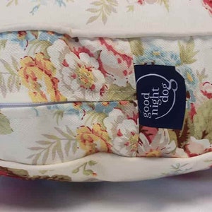 May include: A white and cream floral patterned dog bed with a zipper closure and a blue label that says "good night dog".