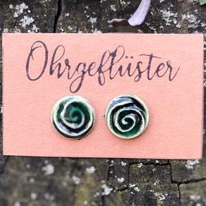 Könnte beinhalten: Ein Paar grüne und weiße Keramikohrringe mit einem Spiraldesign. Die Ohrringe befinden sich auf einer Karte mit der Aufschrift "Ohrgeflüster".