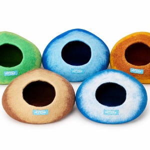 May include: Five rounded pet caves in green, blue, orange, tan, and white-blue gradient colors. Each cave features a circular opening and a small light blue rectangular tag with the text Everest Pet Cave printed in white on the front.