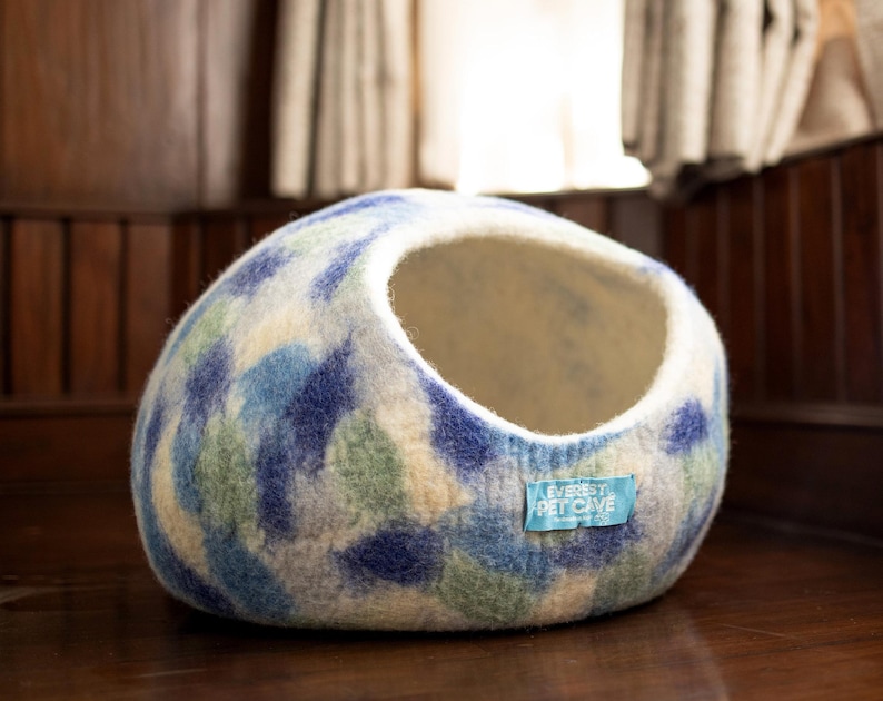 May include: A blue and white patterned felt cat bed with a round shape and a hole for entry. The bed has a label that says "Everest Pet Cave".