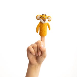 May include: A yellow felt finger puppet shaped like a tiger with brown eyes and a black nose.