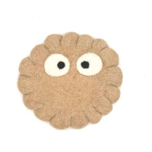 Może przedstawiać: Brązowa podkładka z filcu z dwoma białymi oczami i czarnymi źrenicami. Podkładka ma falisty brzeg.