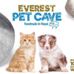 K&ouml;nnte beinhalten: Eine flauschige orangefarbene Katze und ein braun-wei&szlig;er Welpe sitzen vor zwei grauen Filzh&ouml;hlen f&uuml;r Haustiere. Der Text lautet EVEREST PET CAVE Handmade in Nepal und MADE WITH 100% NEWZEALAND WOOL. Der Hintergrund ist wei&szlig; und die Artikel sind aus Wolle.