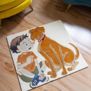 Op de afbeelding: Een wit tapijt met een cartoonillustratie van een jongen en een bruine hond. De jongen draagt een blauw shirt en een oranje broek. De hond draagt een rode halsband.