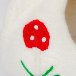 May include: A white felt mushroom-shaped cat bed with a red mushroom cap and a red mushroom on the side. The mushroom has three white dots. Green leaves are embroidered at the base. A whimsical and cozy pet accessory.